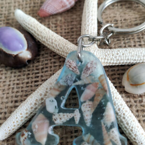 denizin dinginliğini cebinizde taşıyın. bu seri, açık mavi pigmentle renklendirilmiş uv dirençli epoksi içinde gerçek minyatür deniz kabukları ve ince sahil kumu kullanılarak tek tek elde üretilir. her harf dökümden önce kompozisyon olarak hazırlanır; kabarcık kontrolü yapılarak dökülür, kürünü tamamladıktan sonra ıslak zımpara → parlatma aşamalarından geçer. sonuç; cam berraklığında, pürüzsüz ve sağlam bir sahil temalı anahtarlık. benzersizlik bildirimi • fotoğraflar örnek kompozisyonlardır; kabuk türü, dizilimi ve kum dokusu doğası gereği her parçada kısmen farklıdır. • gönderilecek ürün, renk tonu ve tema olarak aynı olmakla birlikte tektir; seri üretim değildir. • her parça paketleme öncesi optik berraklık, yüzey kalitesi ve halka/klips sağlamlığı açısından kalite kontrolden geçirilir. malzeme & işçilik • reçine: sararmaya karşı güçlendirilmiş iki bileşenli epoksi, açık mavi (lagün) pigment. • İçerik: gerçek deniz kabukları (çeşitli minyatür türler) + ince taneli kum. • metal aksam: nikel renkli halka ve zincir. • boyut (yaklaşık): harfe göre 4–5 cm yükseklik; halka ile toplam uzunluk 9–11 cm. • ağırlık: 12–20 g (harf ve kompozisyona göre değişir). kullanım & bakım • kimyasal deterjan ve alkol bazlı temizleyiciden uzak tutun; gerektiğinde yumuşak, kuru bezle silin. • epoksi cam benzeri serttir; aşırı darbe ve yüksek ısıdan kaçınınız. • havuz/deniz sonrası metal aksamın ömrü için kurulayınız. paketleme • her ürün, çizilmeyi önleyen iç kılıf + darbe emici ped ile hediyelik kutu içinde gönderilir. satış notu • mevcut stoktaki harfler satışta aktiftir; listede görünmeyen harfler stokta yoktur. • Özel istek/kişiselleştirme bu seri için yapılmamaktadır.